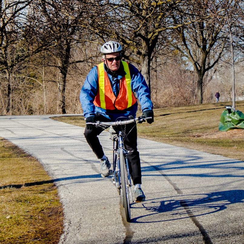 Roads, cycle paths, or towpaths, let's ride where you want to. A cyclist wearing hi-vis clothing, riding through a park.